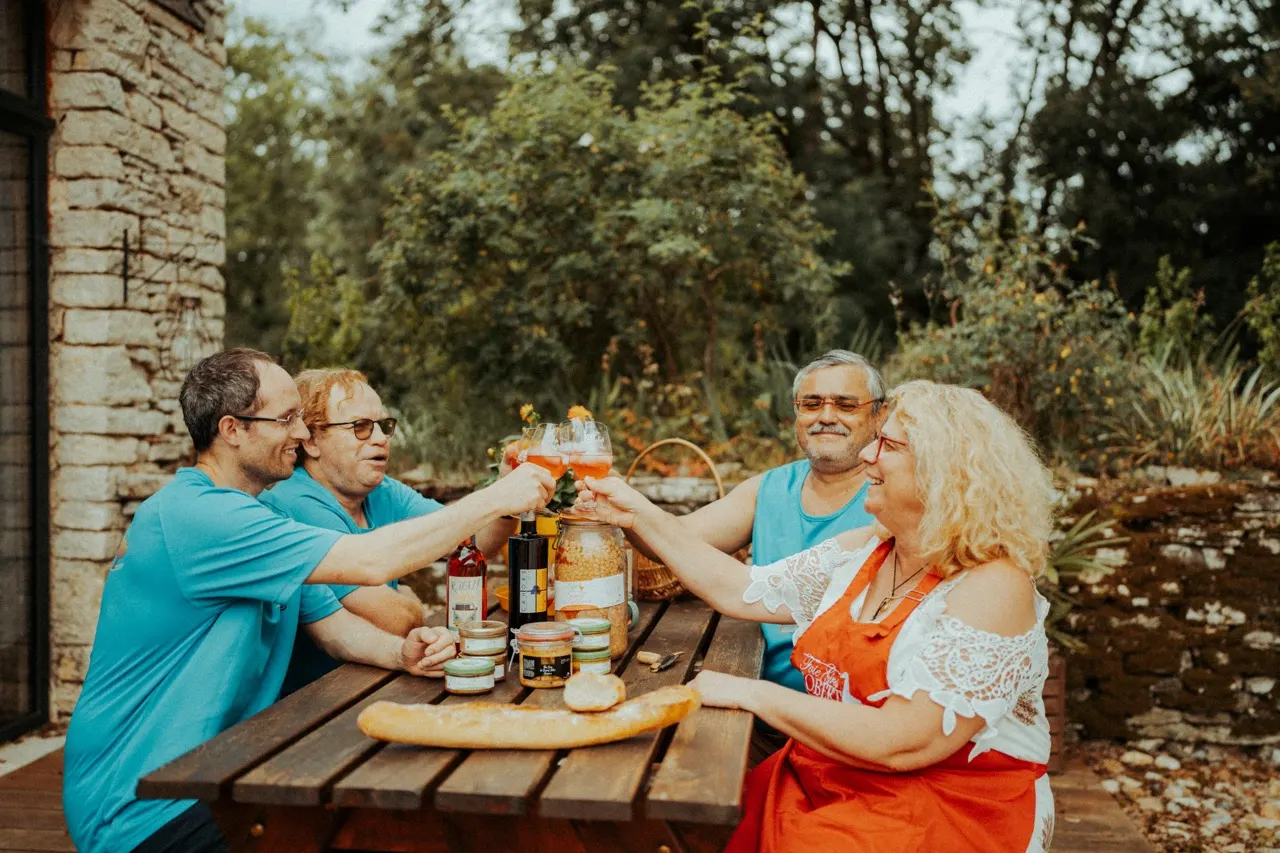L'équipe de la ferme trinque autour d'une table garnie de bocaux, devant un mur de pierre